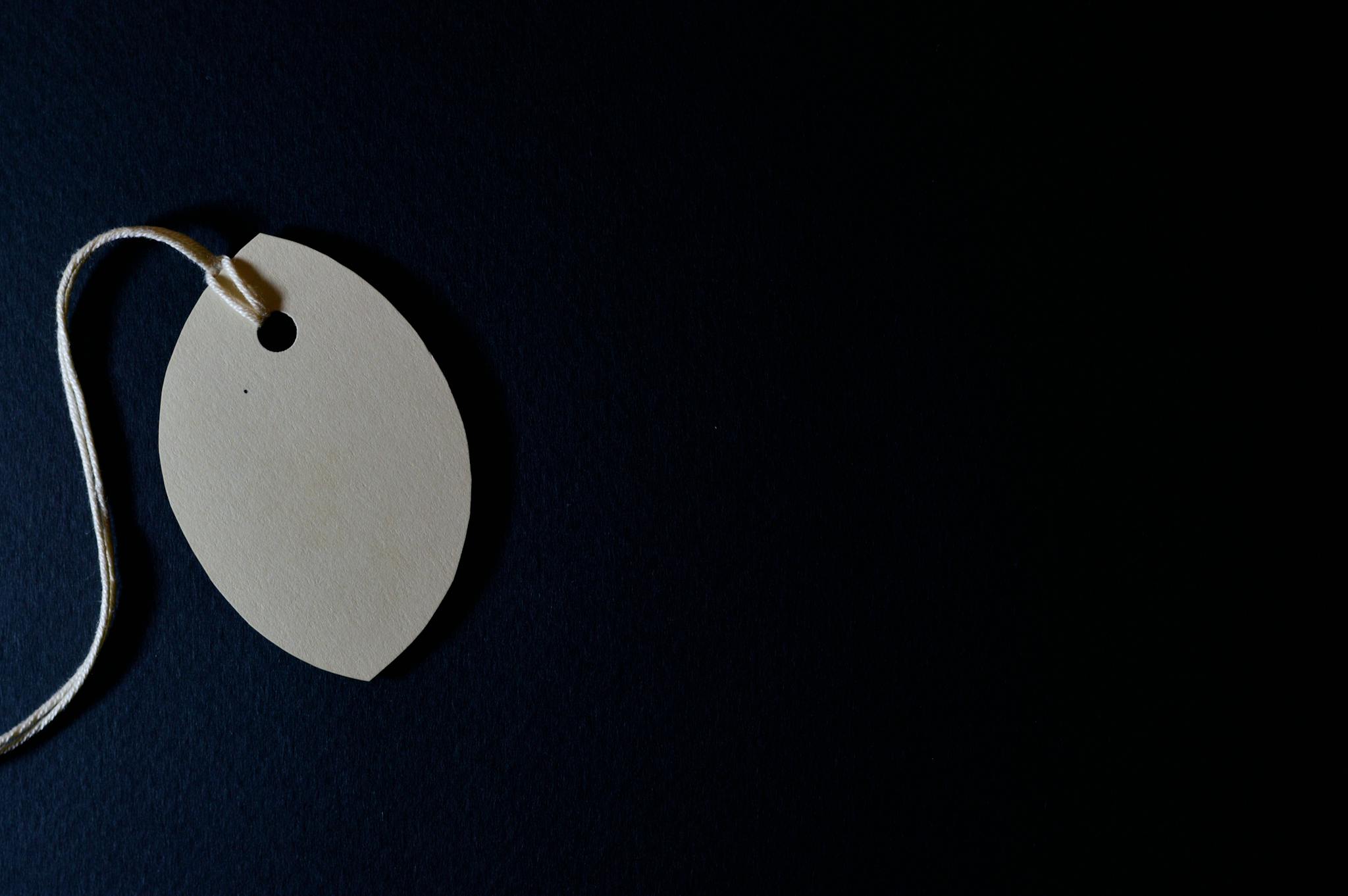 Close-up of a blank paper tag with string on a dark background, perfect for customizable designs.